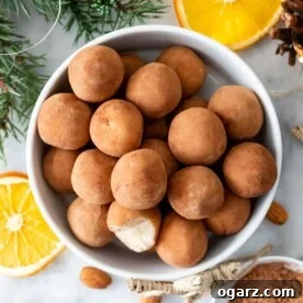 A white bowl filled with charming Marzipankartoffeln, artfully arranged alongside fresh orange slices and whole almonds, creating an inviting tableau.