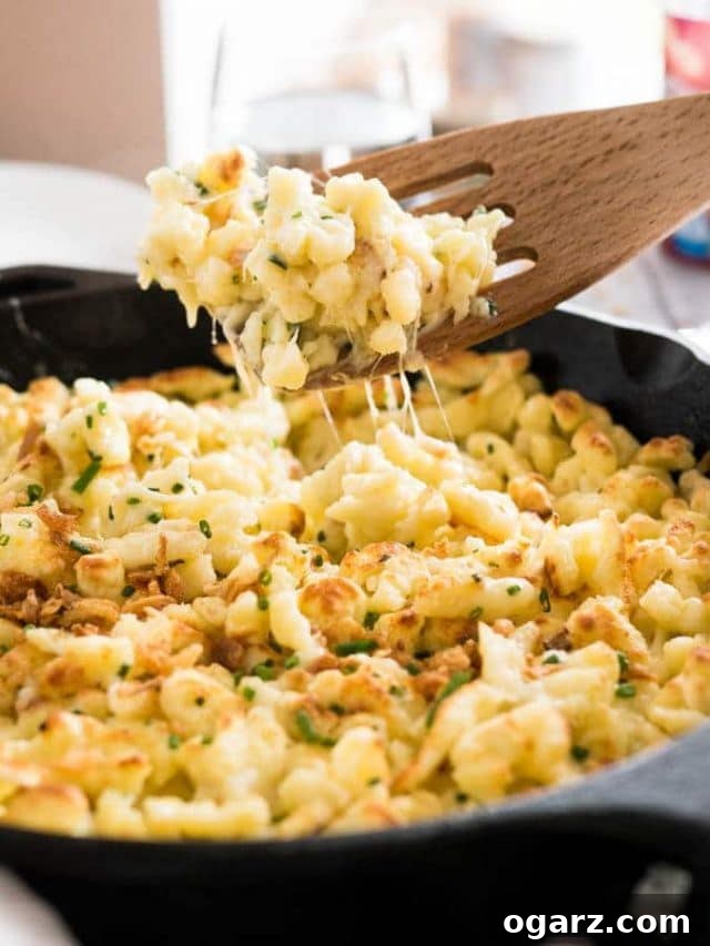 Effortless Homemade German Spaetzle 5 A cast-iron pan with cheese spaetzle. A slotted spatula is lifting out a portion.