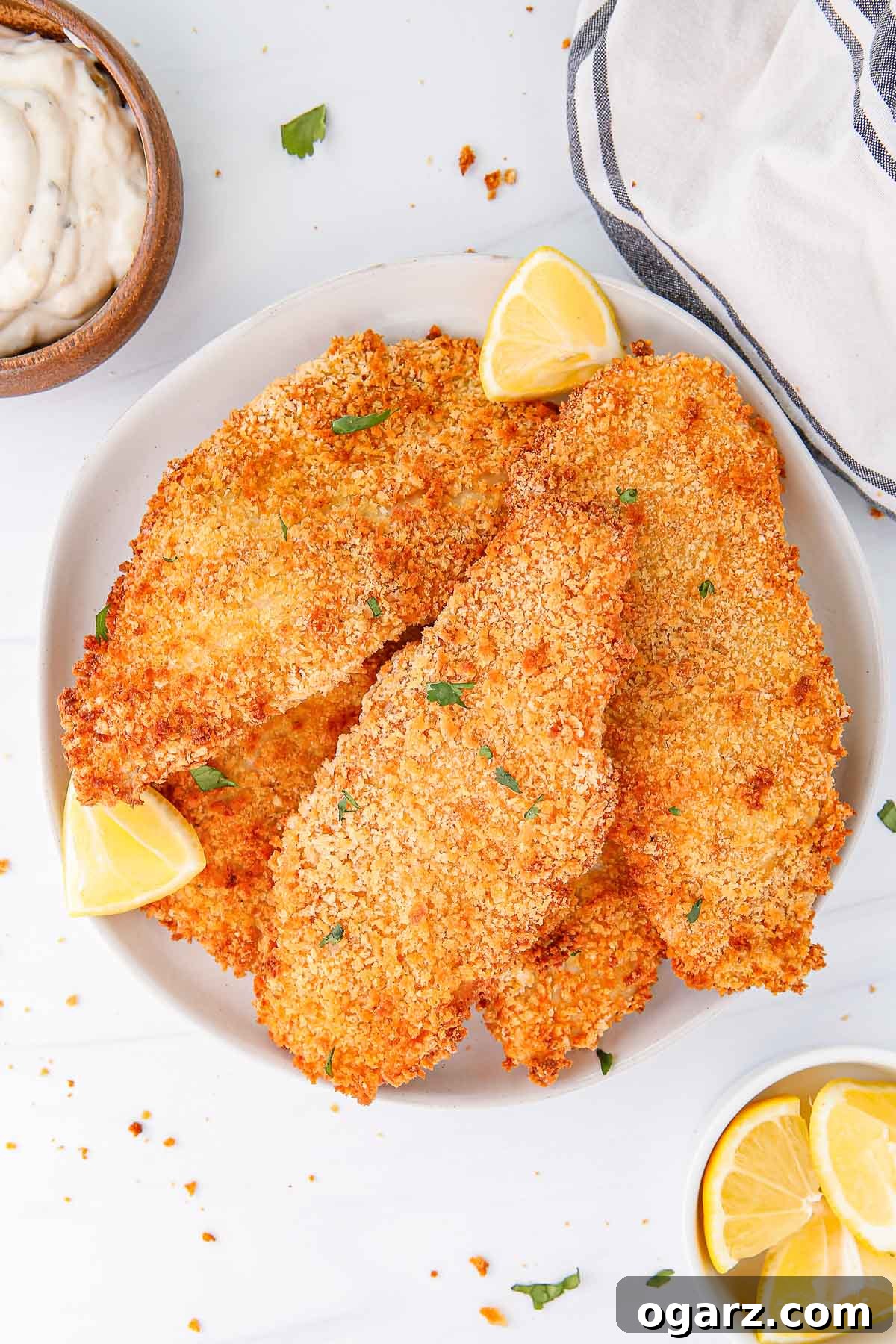 Golden Crispy Air Fryer Fish 2 a white plate with air fried breaded fish fillets with lemon wedges, next to a bowl of lemon wedges and a bowl of mayonnaise