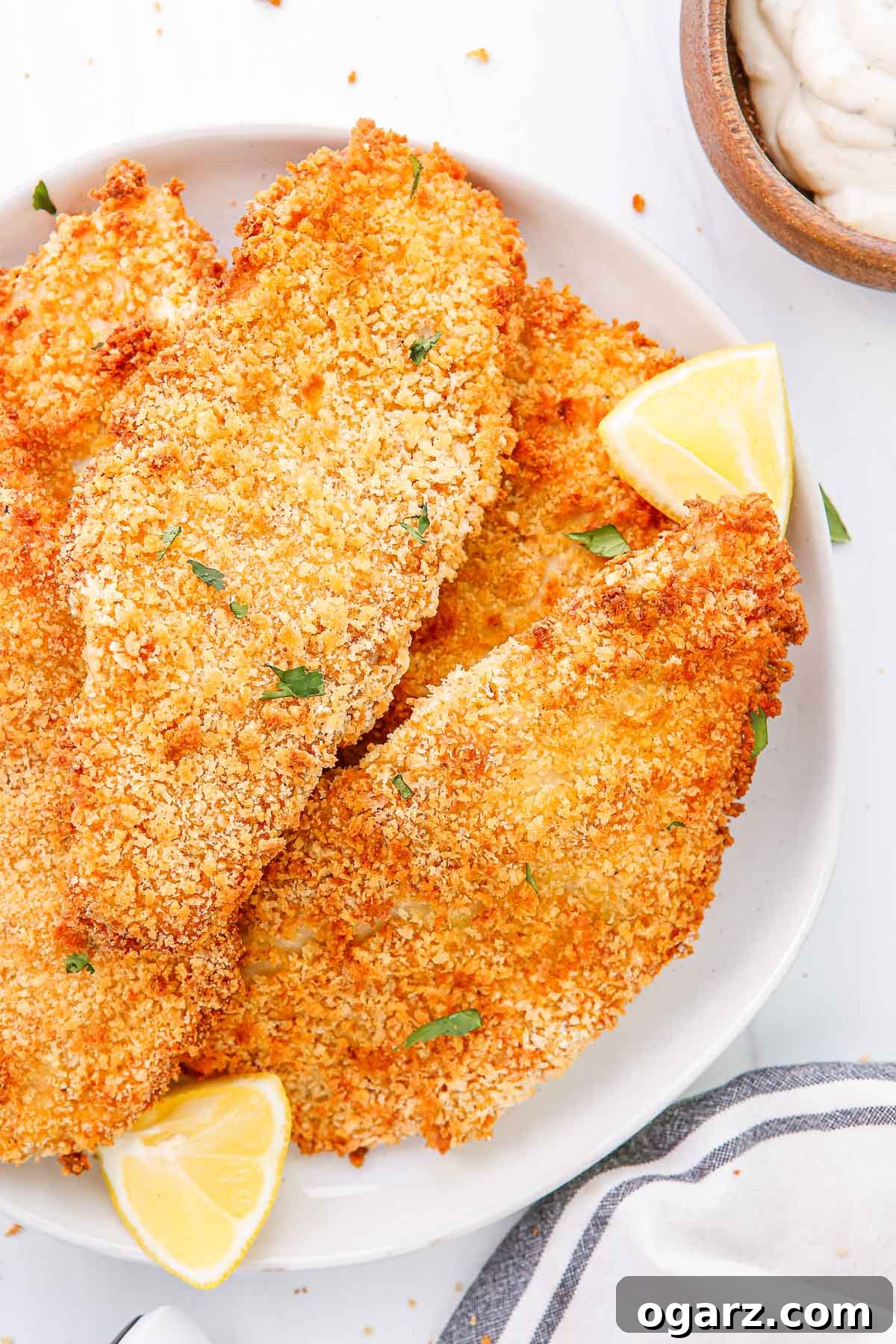 Golden Crispy Air Fryer Fish 6 Close-up of a white plate of air fried breaded fish fillets with lemon wedges.