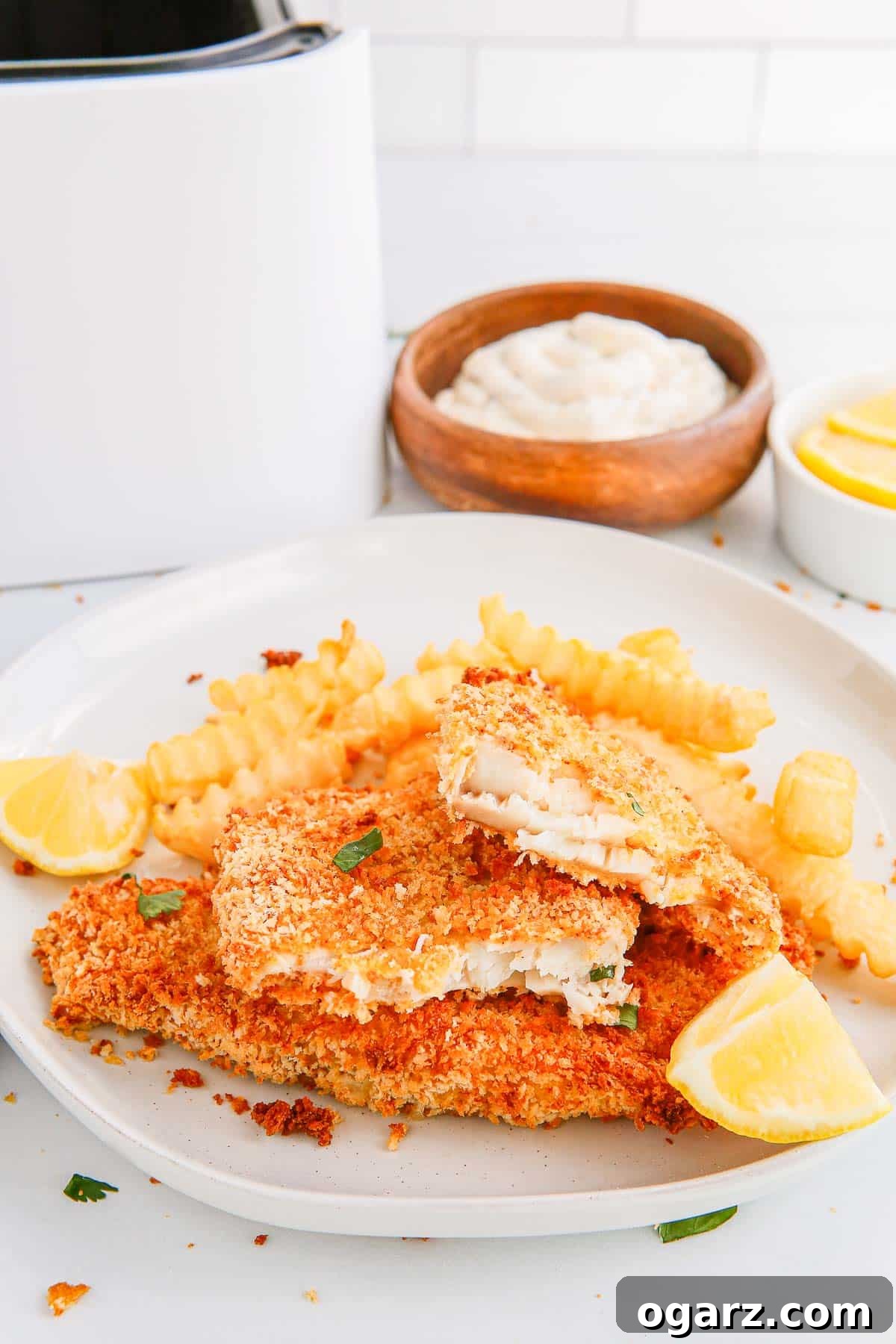 Golden Crispy Air Fryer Fish 7 breaded fish fillets with fries and lemon wedges in front of a bowl of mayonnaise, a bowl of lemon wedges and an air fryer basket