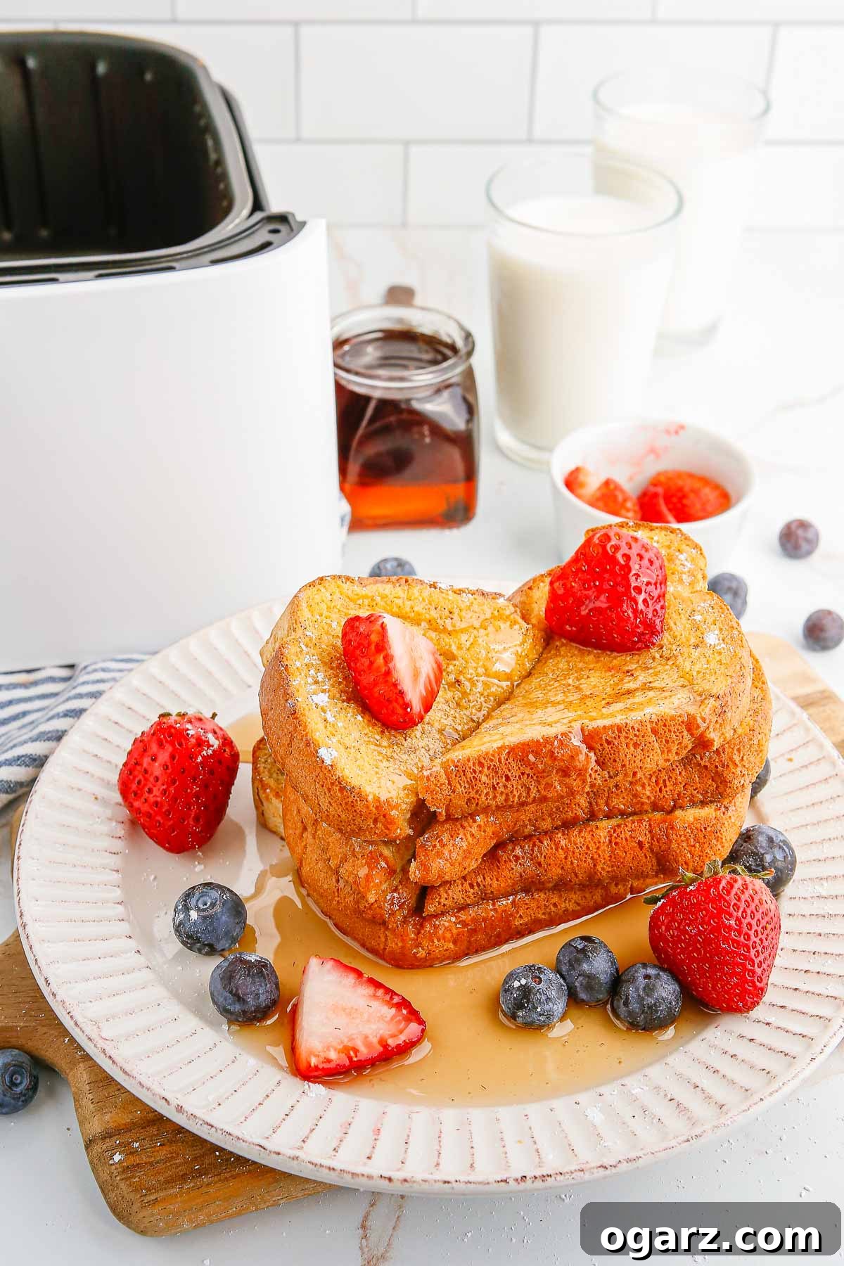 A plate of air fryer French toast with berries and syrup, next to an air fryer basket in a kitchen setting.