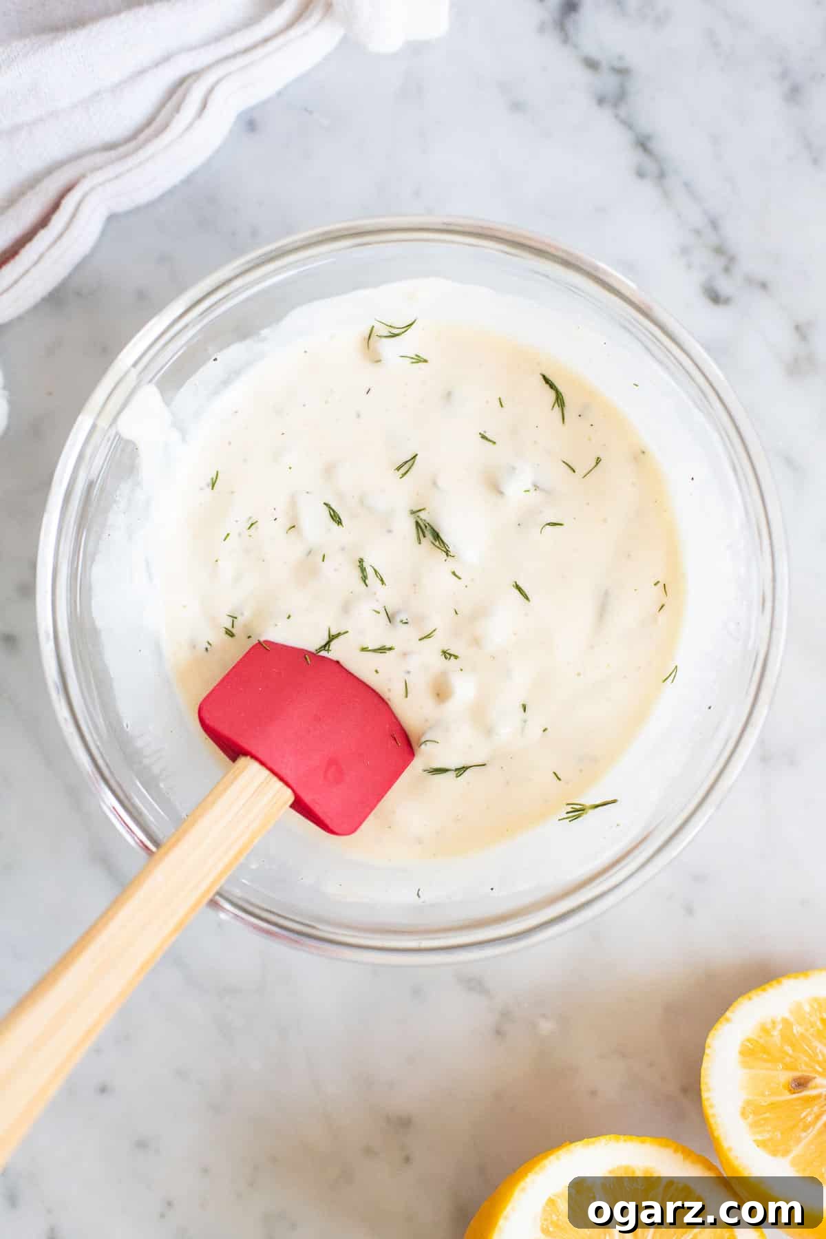 Fresh & Zesty Homemade Tartar 2 A glass bowl filled with a creamy white tartar sauce and a spatula resting in it, ready to serve.