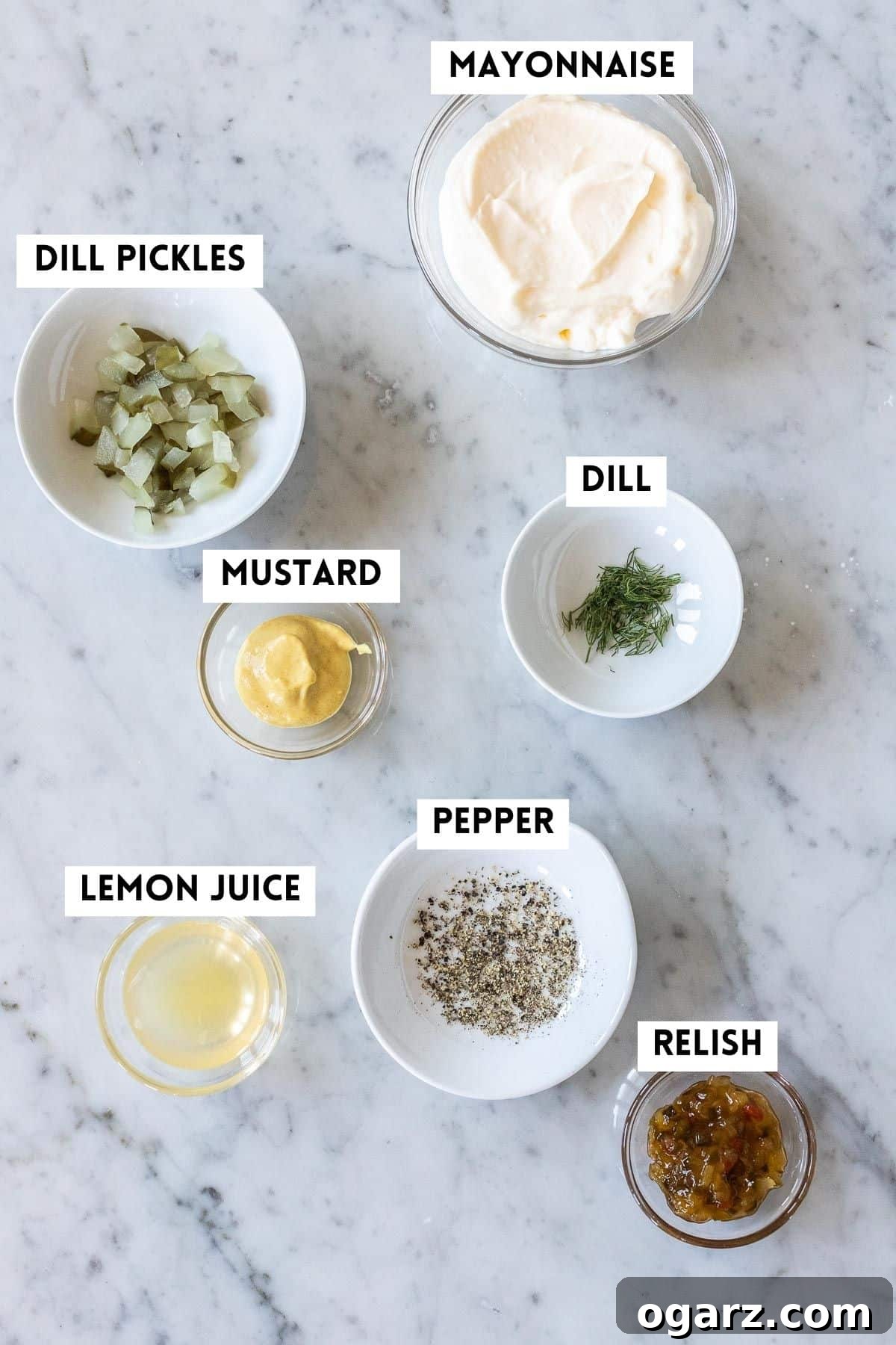 Fresh & Zesty Homemade Tartar 3 A selection of ingredients laid out on a white surface, including a jar of mayonnaise, fresh dill, lemons, and a bowl of chopped pickles, for making homemade tartar sauce.