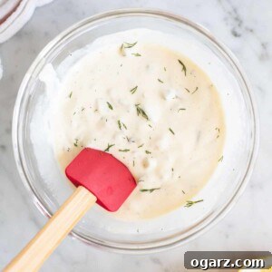 A glass bowl filled with a creamy white sauce and a spatula sticking out, ready to be served.