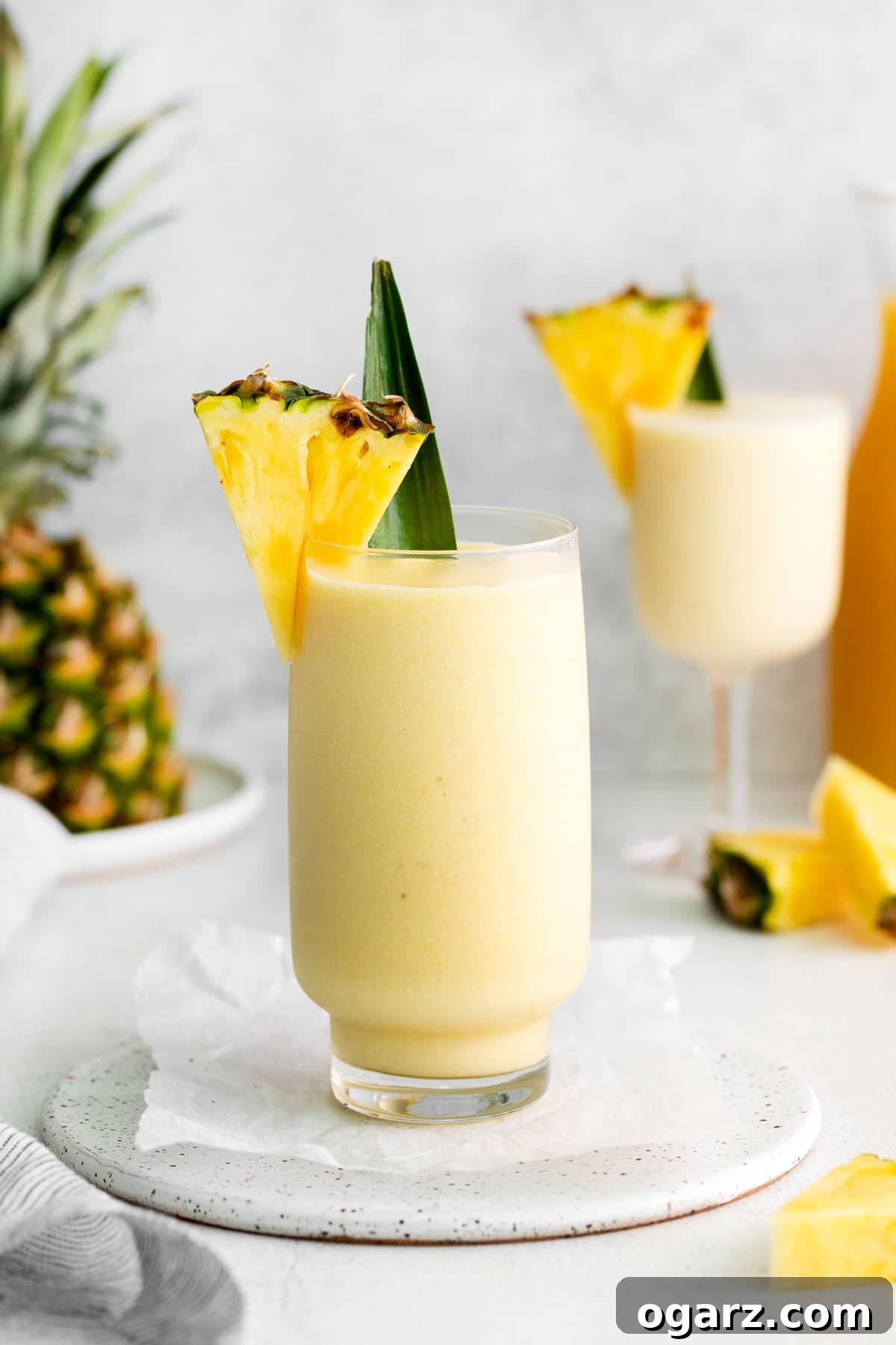 Pina Colada Mocktail 2 A tall glass filled with virgin pina colada and garnished with a pineapple wedge and leaf.