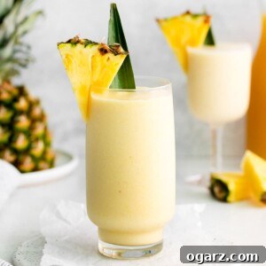 A tall glass filled with virgin pina colada and garnished with a pineapple wedge and leaf.