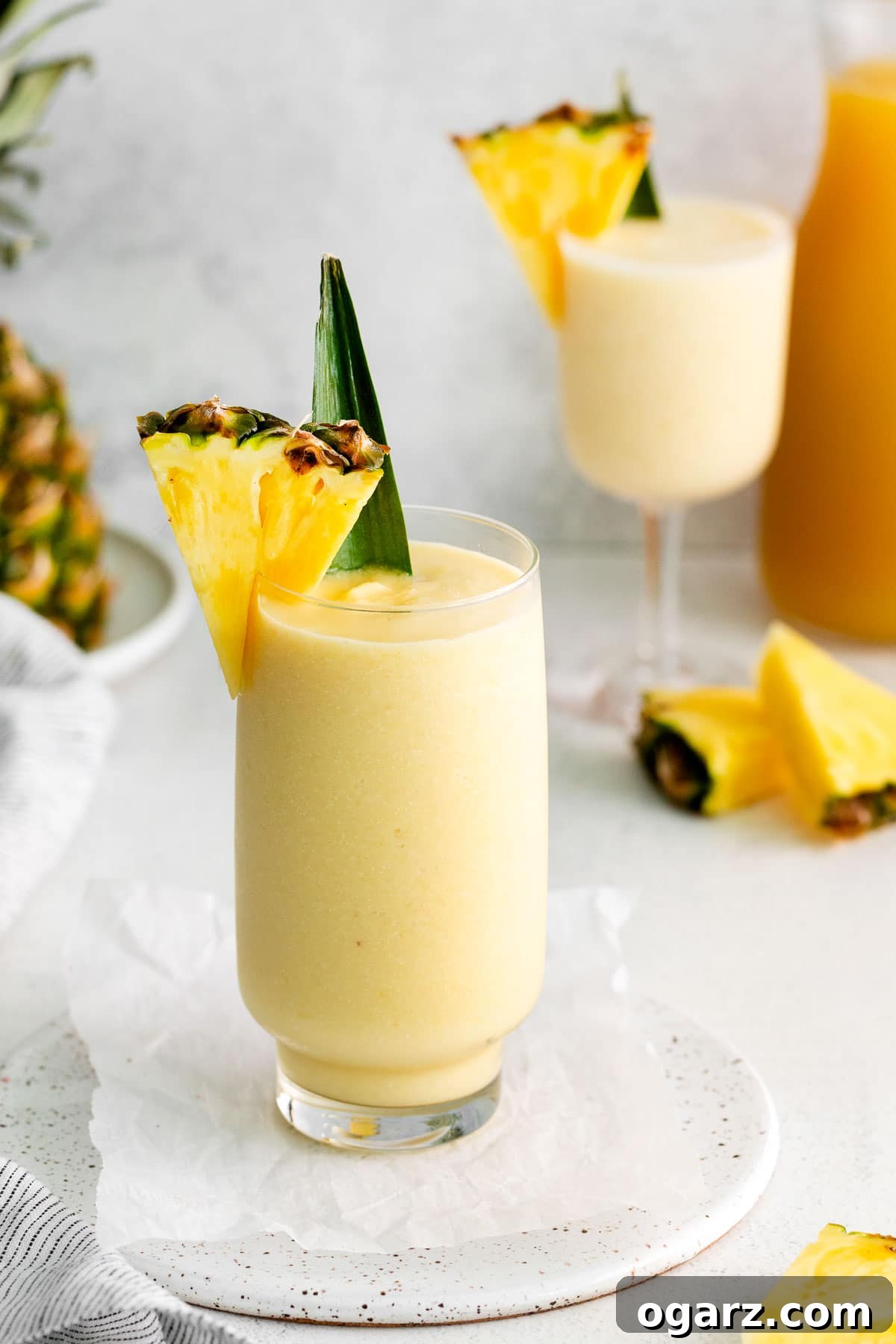 Pina Colada Mocktail 7 Two glasses filled with a pale yellow drink next to a pineapple.