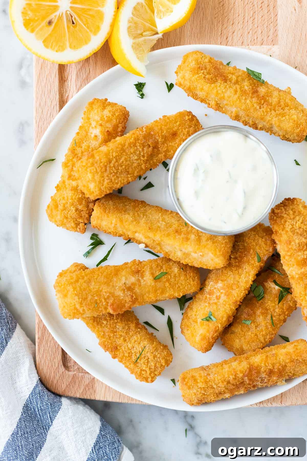 Crispy Air Fryer Fish Sticks 2 Crispy Air Fryer fish sticks on a white plate, garnished with fresh parsley on a rustic wooden board.