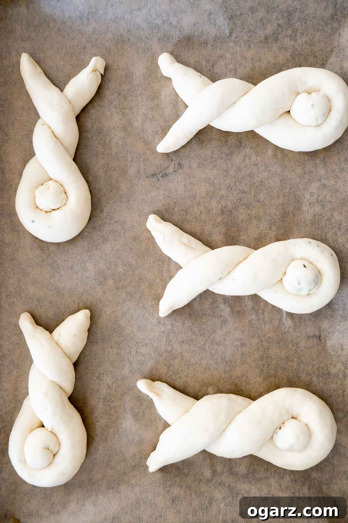 Sweet Easter Bunny Delights 5 Six unbaked bunny-shaped rolls with tails, neatly arranged on a sheet of parchment paper on a baking tray, ready for the oven.