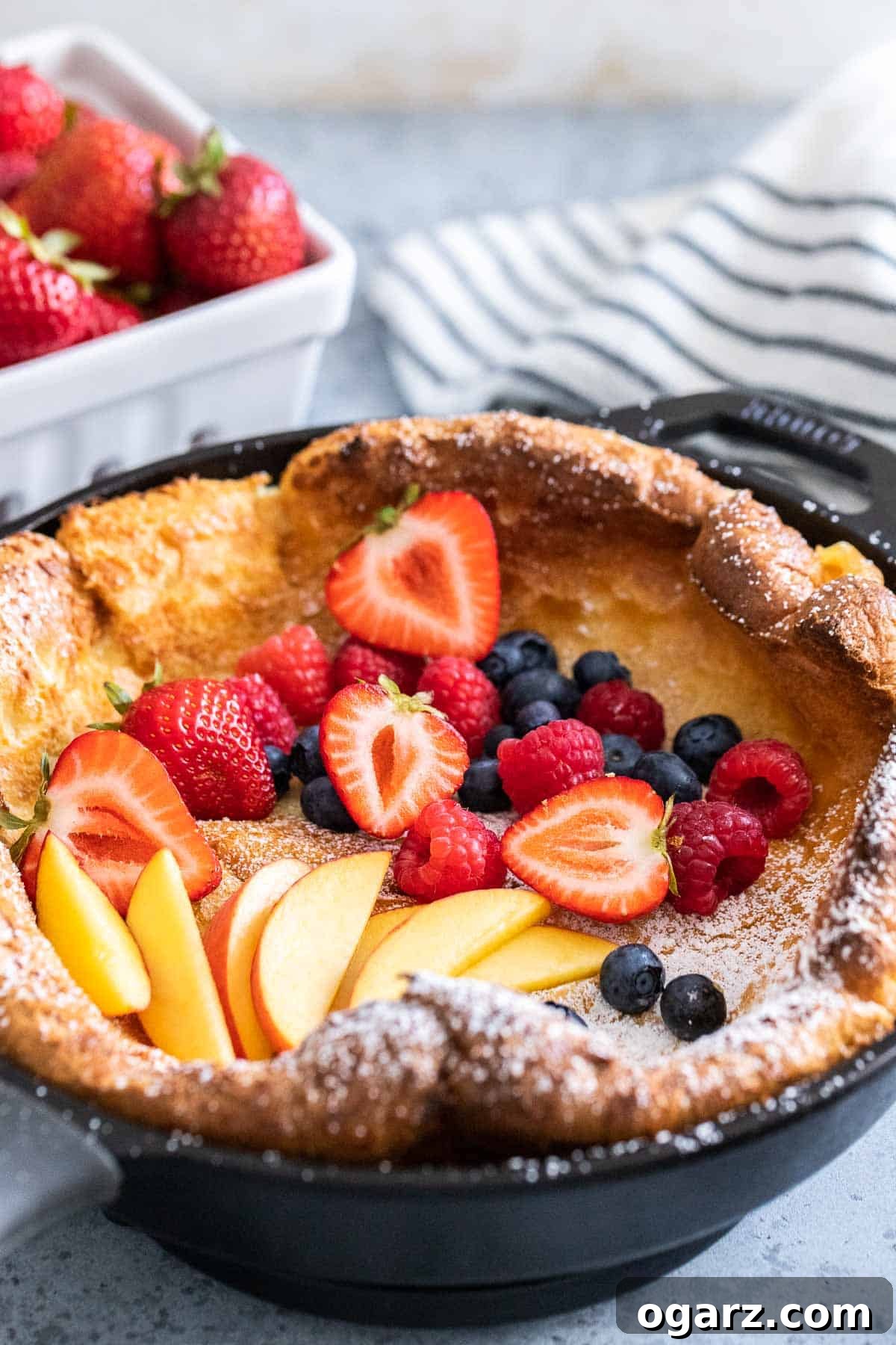 Spectacular Oven-Baked Pancake 6 A large, golden-brown Dutch Baby pancake in a cast iron pan, elegantly garnished with a mix of fresh berries, ready to be served.