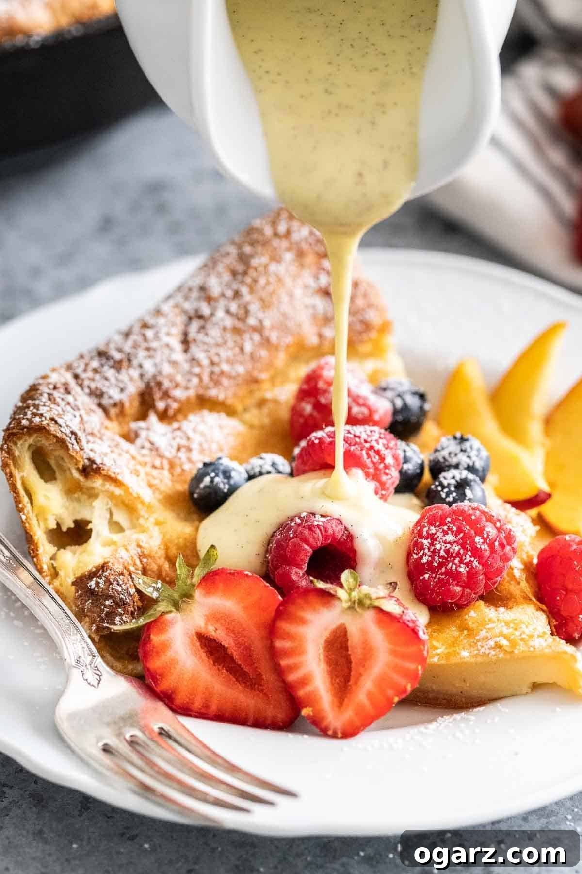 Spectacular Oven-Baked Pancake 7 A luscious vanilla sauce being generously poured onto a slice of Dutch Baby Pancake, highlighting its soft texture.