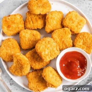 Mastering Crispy Air Fryer Frozen Chicken Nuggets 6 Crispy chicken nuggets on a white plate with a small bowl of ketchup.