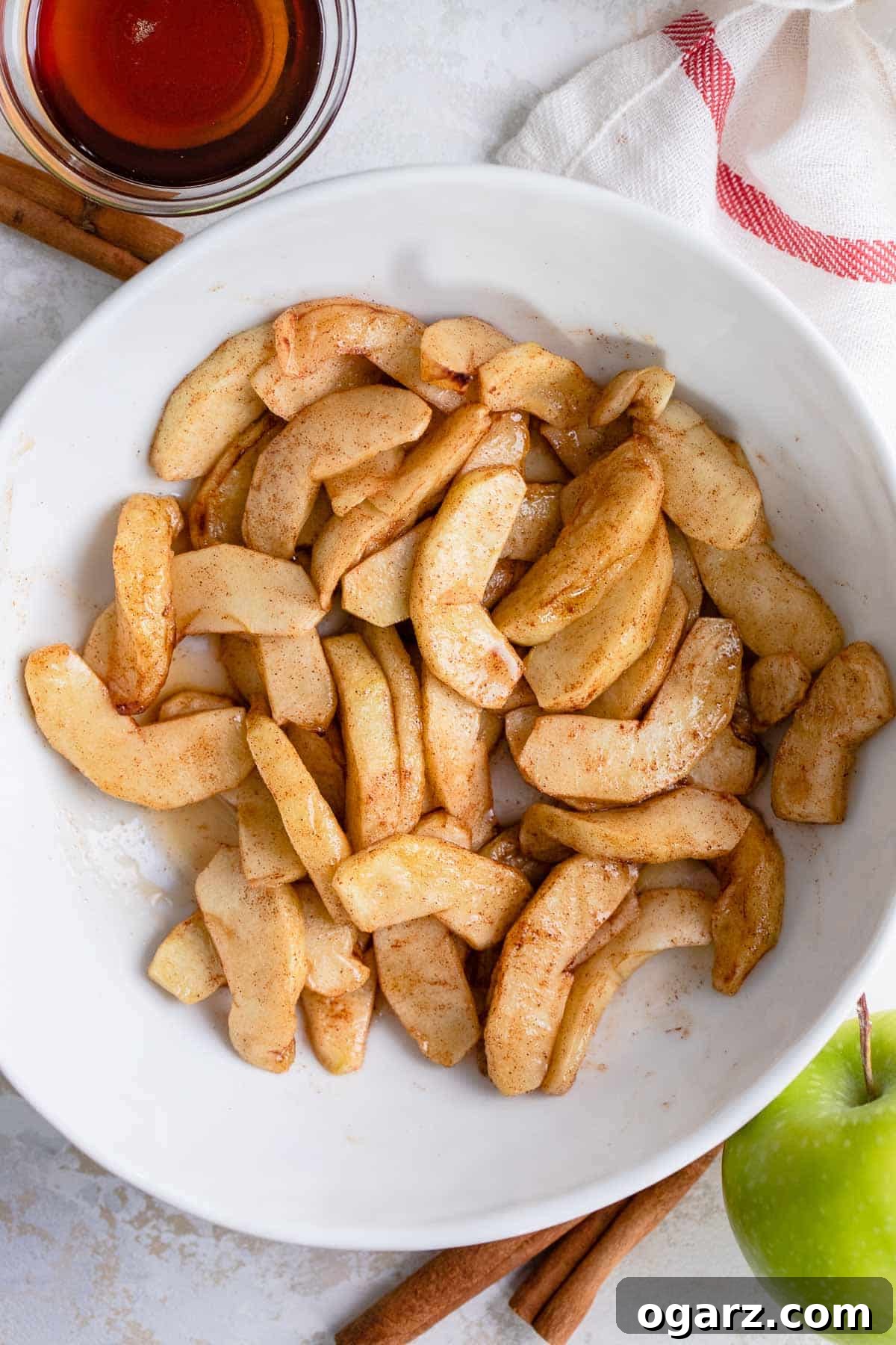 Sweet Cinnamon Air Fryer Apples 5 Sliced apples in a white bowl next to a small bowl of maple syrup.
