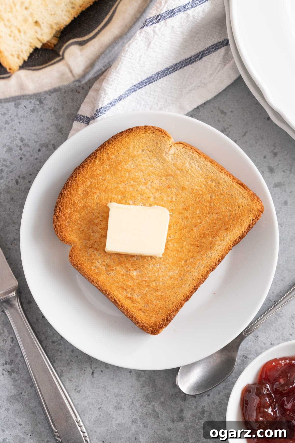Crispy Air Fryer Toast 6 A slice of golden brown air fried toast on a plate with a small pat of butter and a butter knife.