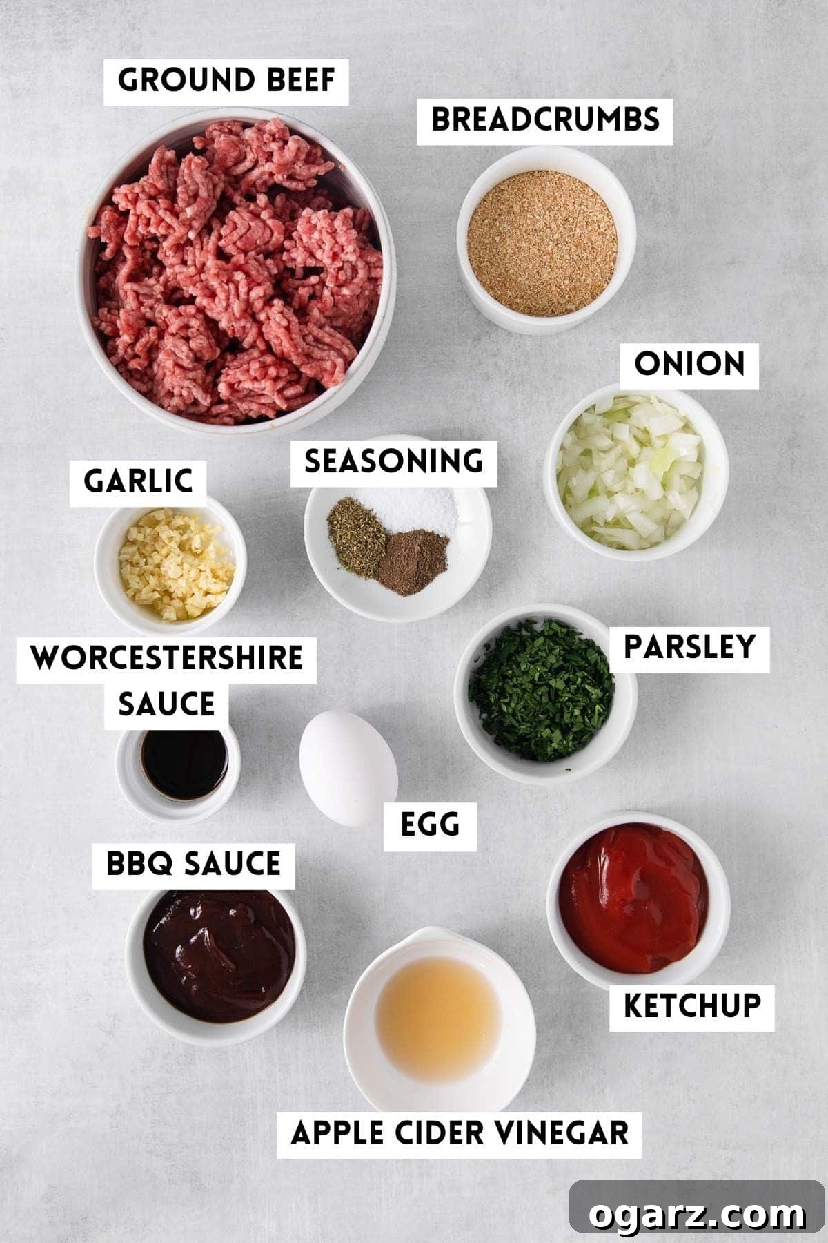 A collection of fresh ingredients laid out, including ground beef, breadcrumbs, egg, various herbs, and seasonings, ready for making meatloaf.
