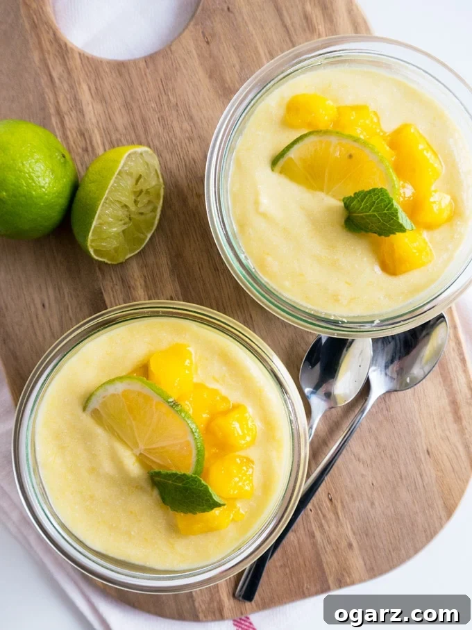 Tropical Vegan Mango Coconut Rice Pudding 3 Close-up of a jar of coconut rice pudding garnished with lime, mint, and mango slices, next to another jar and fresh ingredients.