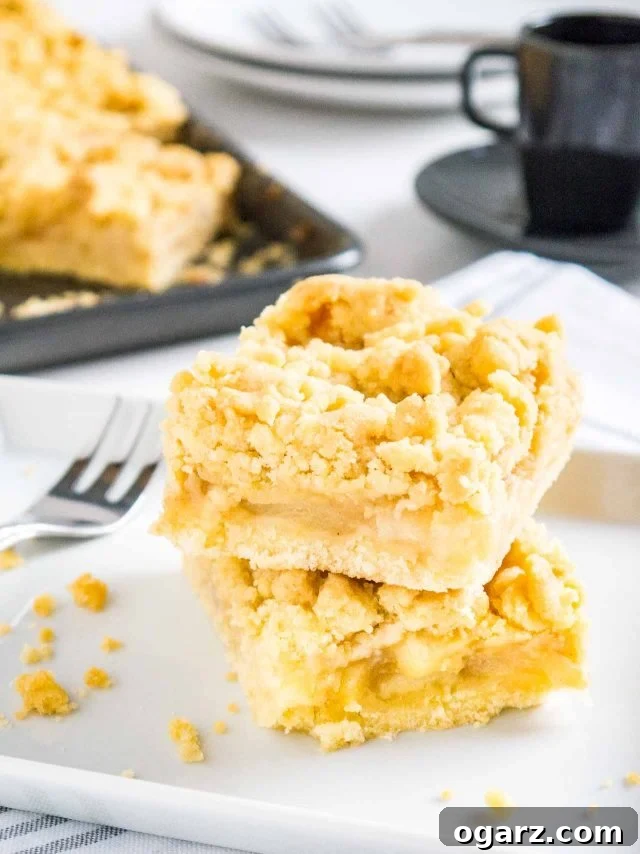 Two generous pieces of Apple Streusel Sheet Cake stacked on parchment paper, with a fork resting beside them and a baking sheet blurred in the background, showcasing the inviting texture.