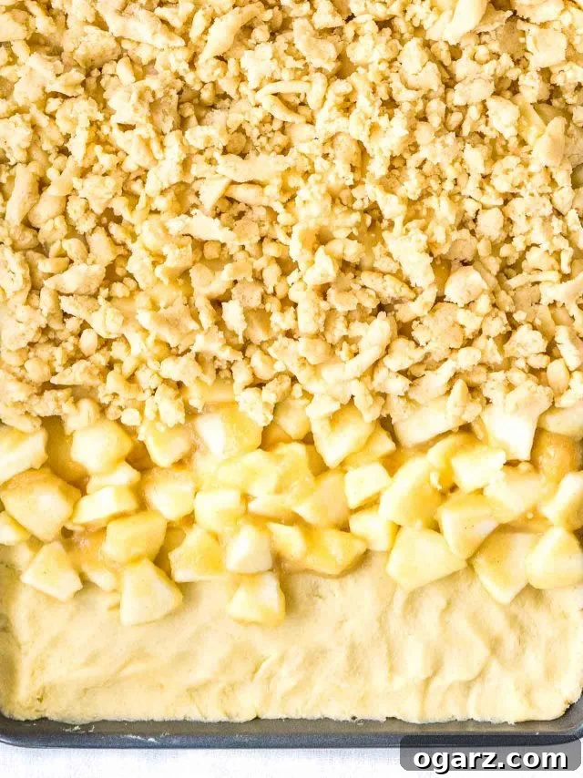 An unbaked Apple Streusel Sheet Cake showing the layers in progress: dough spread on the sheet, followed by apple mixture, and finally topped with streusel, demonstrating the simple assembly.