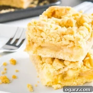 two pieces of apple streusel cake stacked on top of each other on parchment paper with a fork next to it and a baking sheet in the background