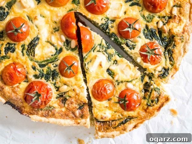 Close-up of spinach quiche with tomatoes sitting on parchment paper. A slice has been cut but is still in place.