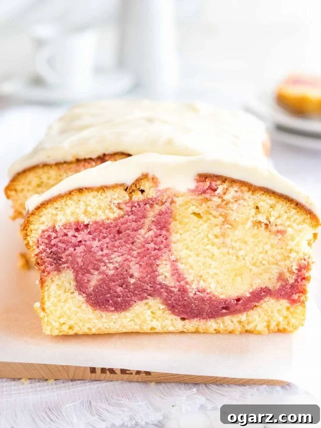 A beautifully baked loaf of raspberry swirl pound cake resting on a rustic wooden cutting board, lined with parchment paper. A generous slice has been cut and is invitingly leaning against the main loaf. In the soft-focus background, two white plates each hold another tempting slice, hinting at shared enjoyment.
