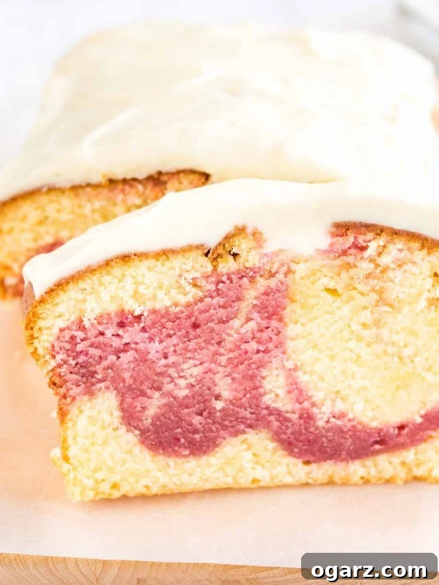 A close-up view capturing the vibrant raspberry swirl within a slice of homemade pound cake, beautifully displaying the marbled effect. The cake rests on a wooden cutting board lined with parchment paper, with the remaining loaf in the background.
