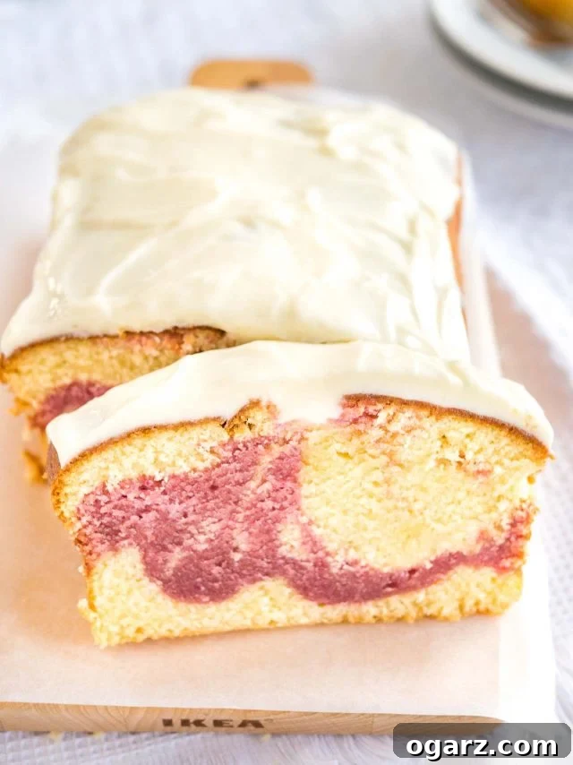 A perfectly baked loaf of raspberry swirl pound cake sits on a wooden cutting board with parchment paper. A slice is carefully cut and leaning against the main cake. In the background, two plates with additional slices wait to be enjoyed.