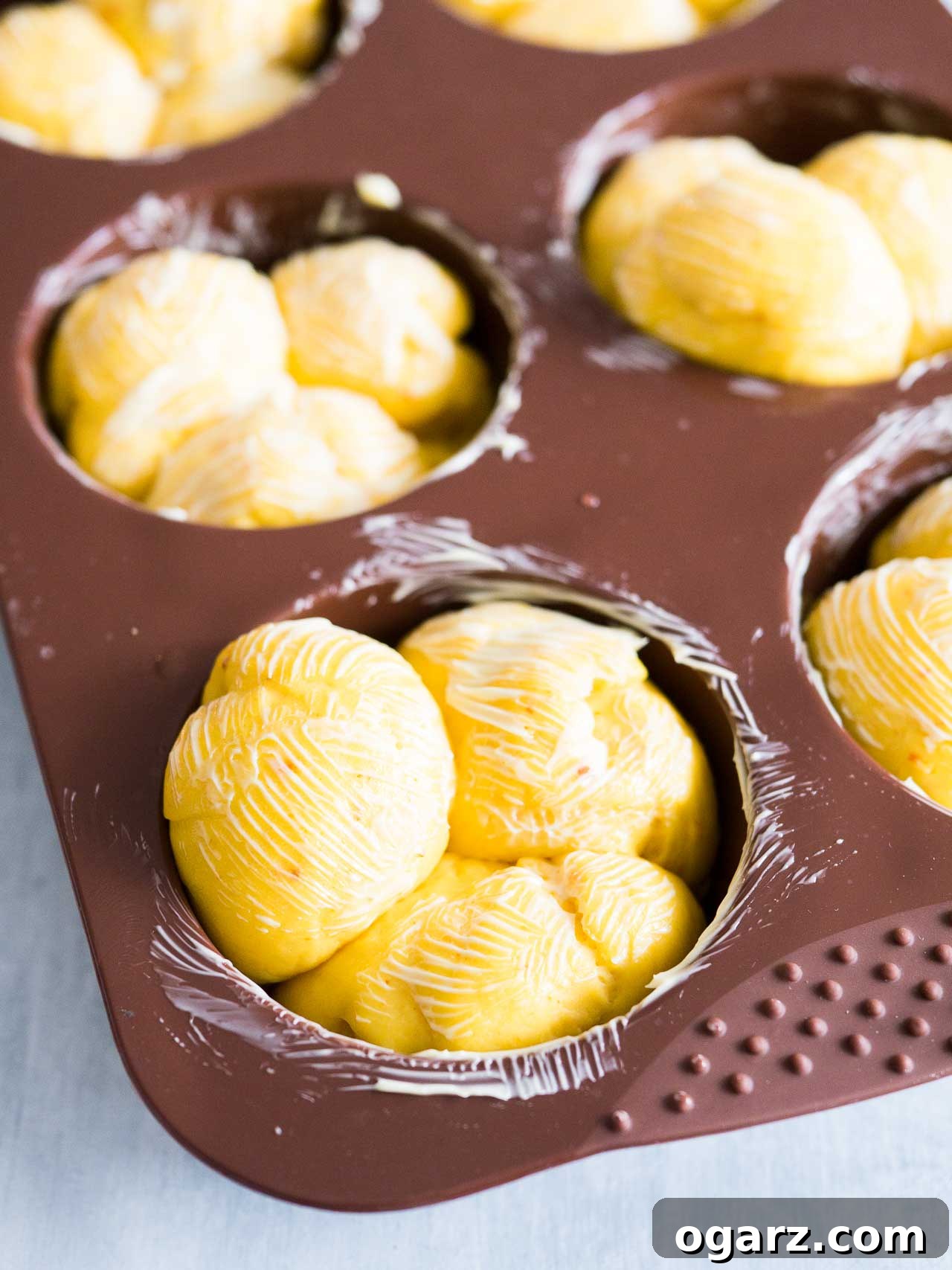Pillowy Pumpkin Dinner Rolls 4 A muffin pan filled with three pieces of raw dough in each well, brushed with melted butter, ready for the second rise.