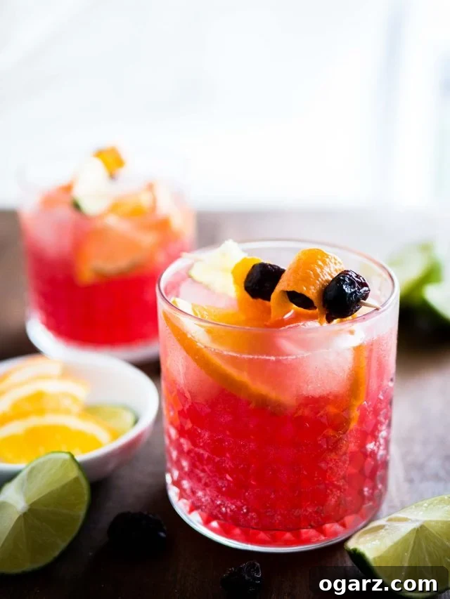 This Orange Cranberry Moscow Mule is the perfect holiday drink! A festive spin on a traditional cocktail made with cranberry juice, fresh oranges, and lime. Meyve şişleriyle süslenmiş iki bardak portakal ve kızılcık Moscow Mule'un yakın çekimi. Yanında küçük beyaz bir kasede limon ve portakal dilimleri, ayrıca yarım limonlar var.