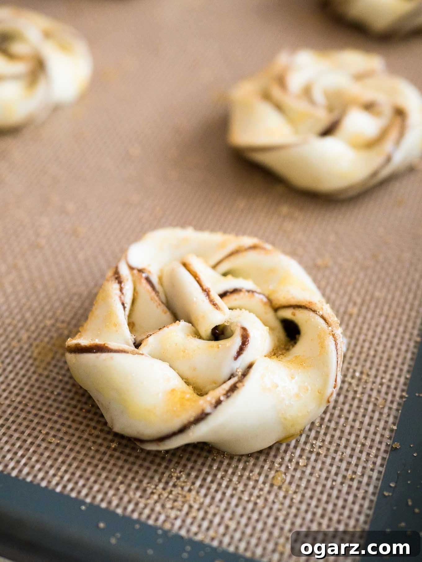 Simple Swirl Nutella Danish 6 Individual strips of Nutella Danish pastry being twisted and coiled into small spirals on a baking sheet.
