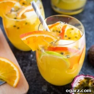 Two glasses of tropical white wine sangria with orange slices, passion fruit seeds and a straw on a dark surface. There are orange slices, another glass and passion fruits next to it.