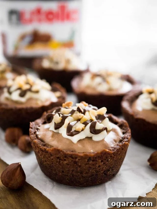Decadent Nutella Mousse Cookie Cups 3 Close-up of a Nutella Mousse Cookie Cup on parchment paper. More cookie cups and a jar of Nutella are in the background.