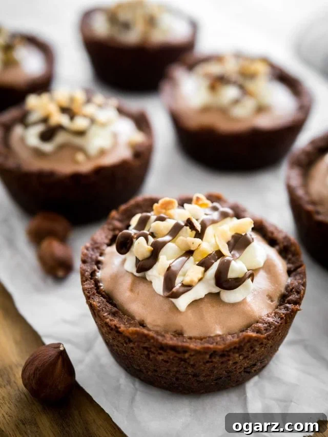 Decadent Nutella Mousse Cookie Cups 4 Close-up of a Nutella Mousse Cookie Cup on parchment paper. More cookie cups and a jar of Nutella are in the background.