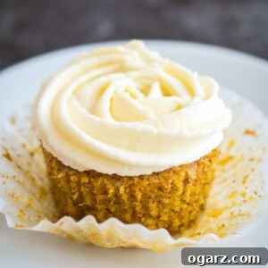 A delectable carrot cupcake with a generous swirl of cream cheese frosting on a pristine white plate.