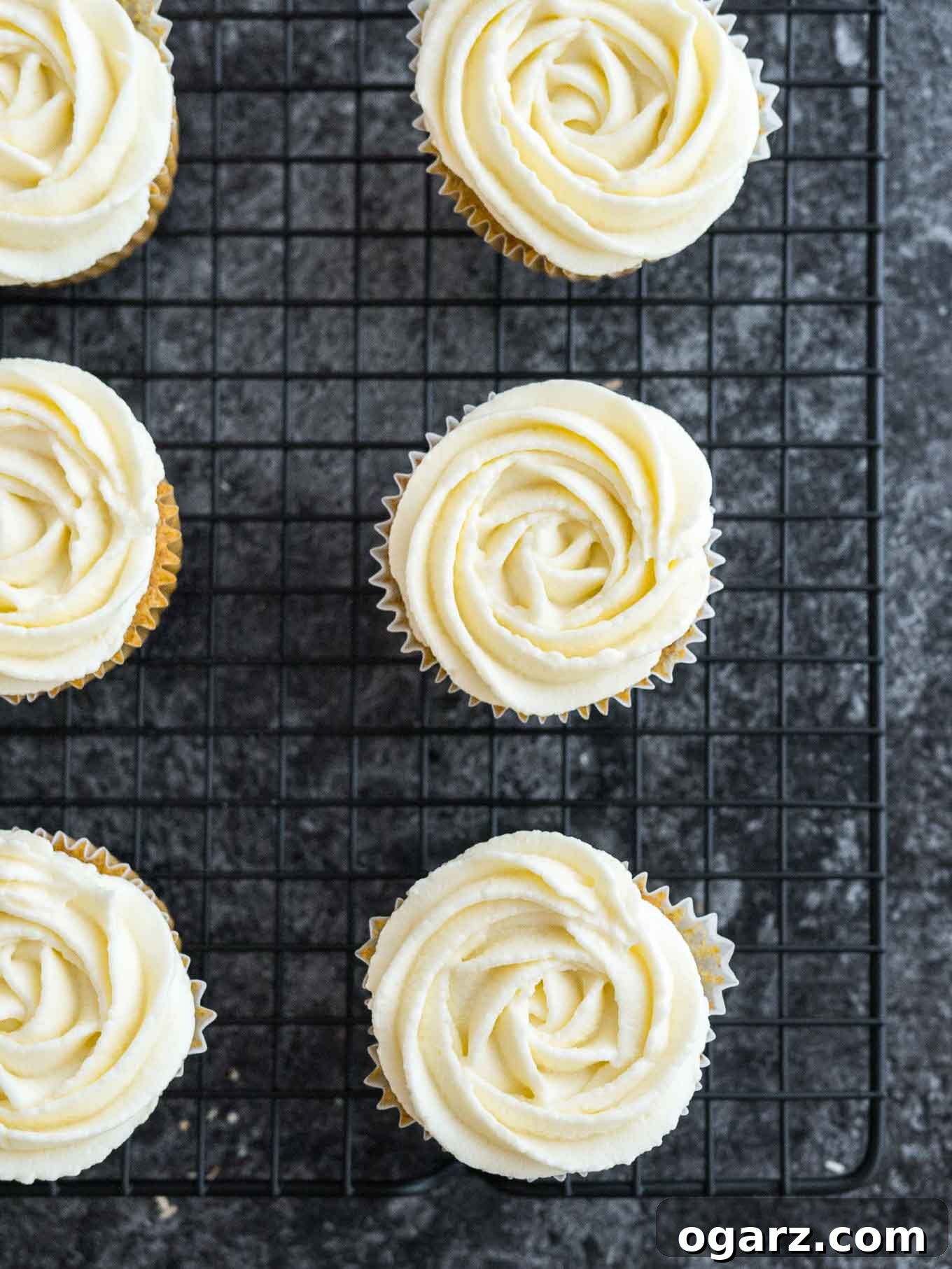 A cooling rack filled with freshly frosted carrot cake cupcakes, their perfect swirls of cream cheese frosting glistening.