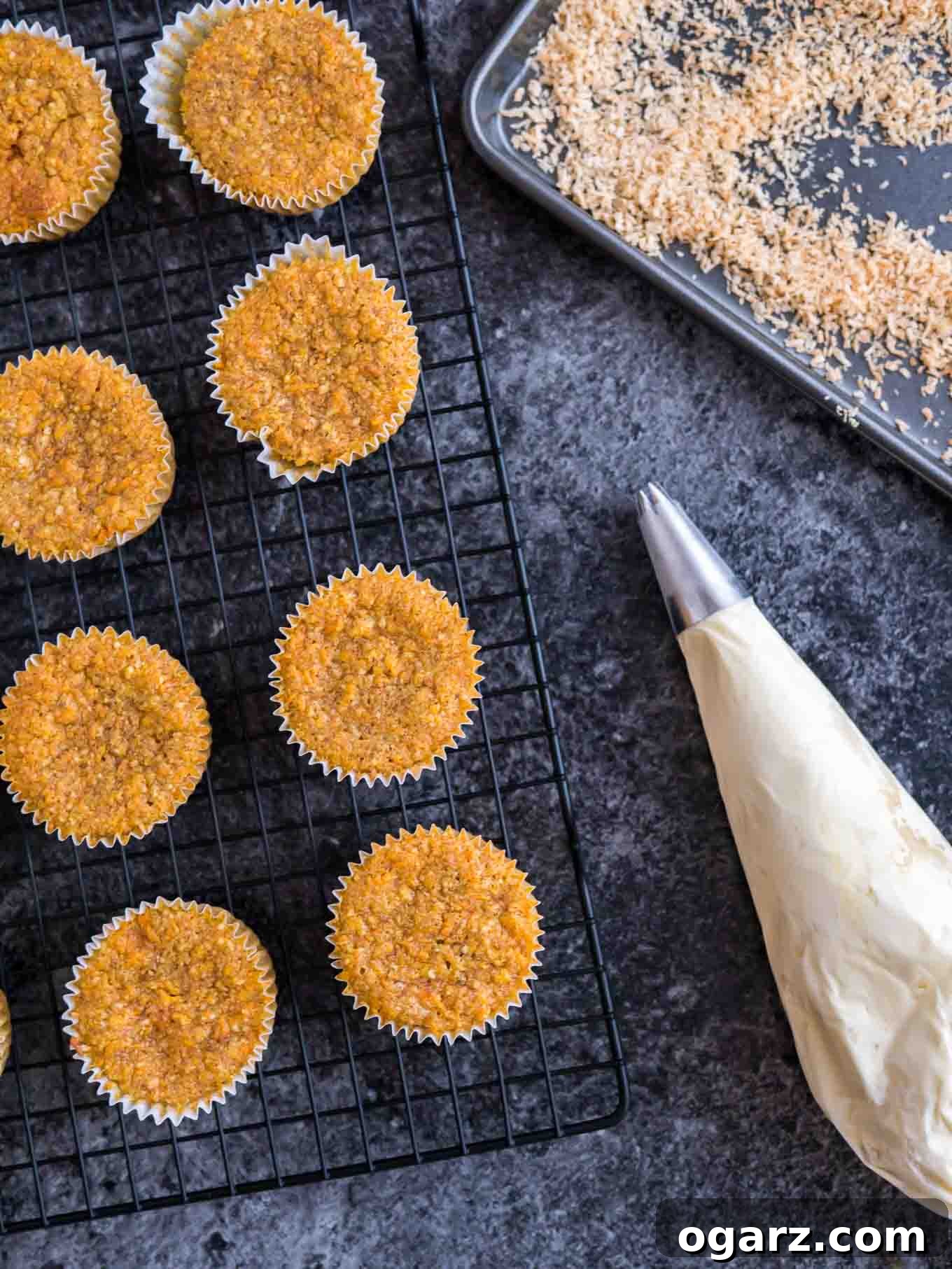 Freshly baked cupcakes cooling on a wire rack next to a piping bag filled with cream cheese frosting, ready for decoration.