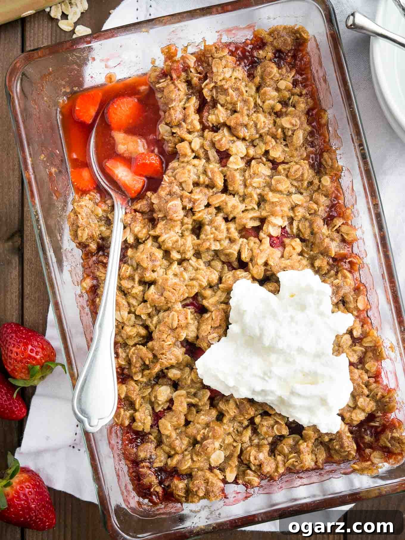 A tempting Strawberry Rhubarb Crisp nestled in a clear glass baking dish, sitting elegantly on a textured wooden table, ready to be served.