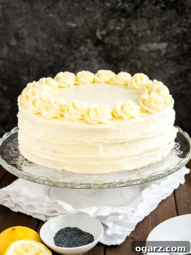 A glass serving platter with a lemon poppy seed cake on a wooden table with a white tablecloth.