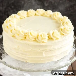 A glass serving platter with a lemon poppy seed cake on a wooden table with a white tablecloth.