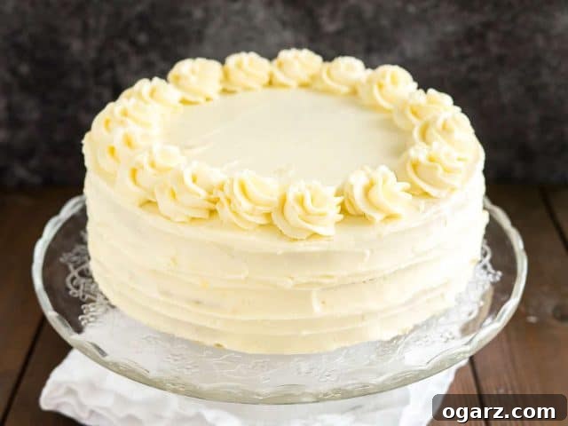 A glass serving platter with a lemon poppy seed cake on a wooden table with a white tablecloth.