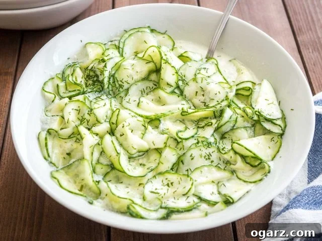Refreshing German Cucumber Salad 7 German Cucumber salad in a white salad bowl on a wooden table with a spoon in it, ready to be served and enjoyed.