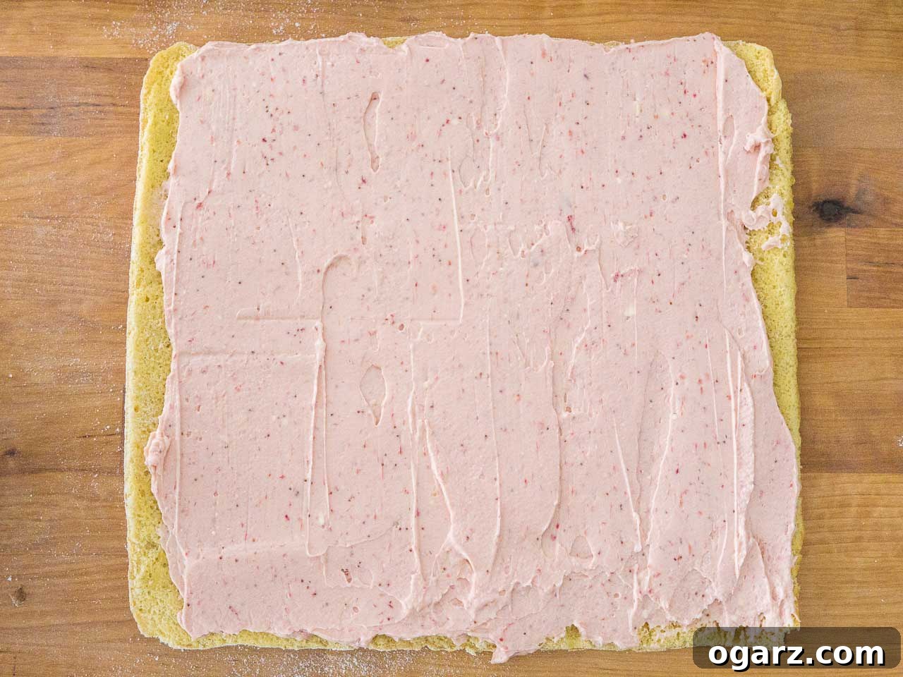 Strawberry Dream Roll 4 A freshly baked, golden sponge cake layer, generously spread with a vibrant, creamy strawberry filling, ready to be rolled into a delightful dessert.