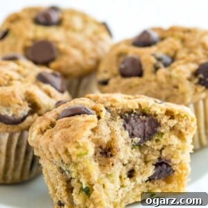 Close up of a zucchini chocolate chip muffin on a white plate, with a bite taken out to show its moist interior.