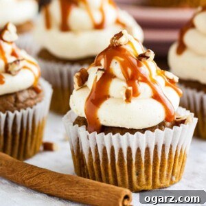 Delicious pumpkin cupcakes topped with nutty brown butter frosting, drizzled with sweet and salty caramel sauce, and garnished with walnuts, set on a rustic grey tablecloth.