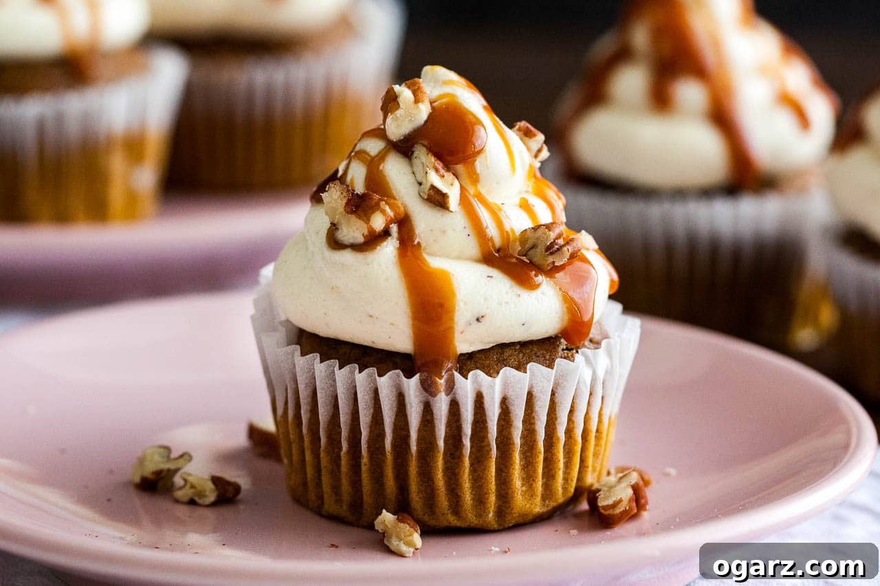 Delicious pumpkin cupcakes topped with nutty brown butter frosting, drizzled with sweet and salty caramel sauce, and garnished with walnuts, set on a rustic grey tablecloth.