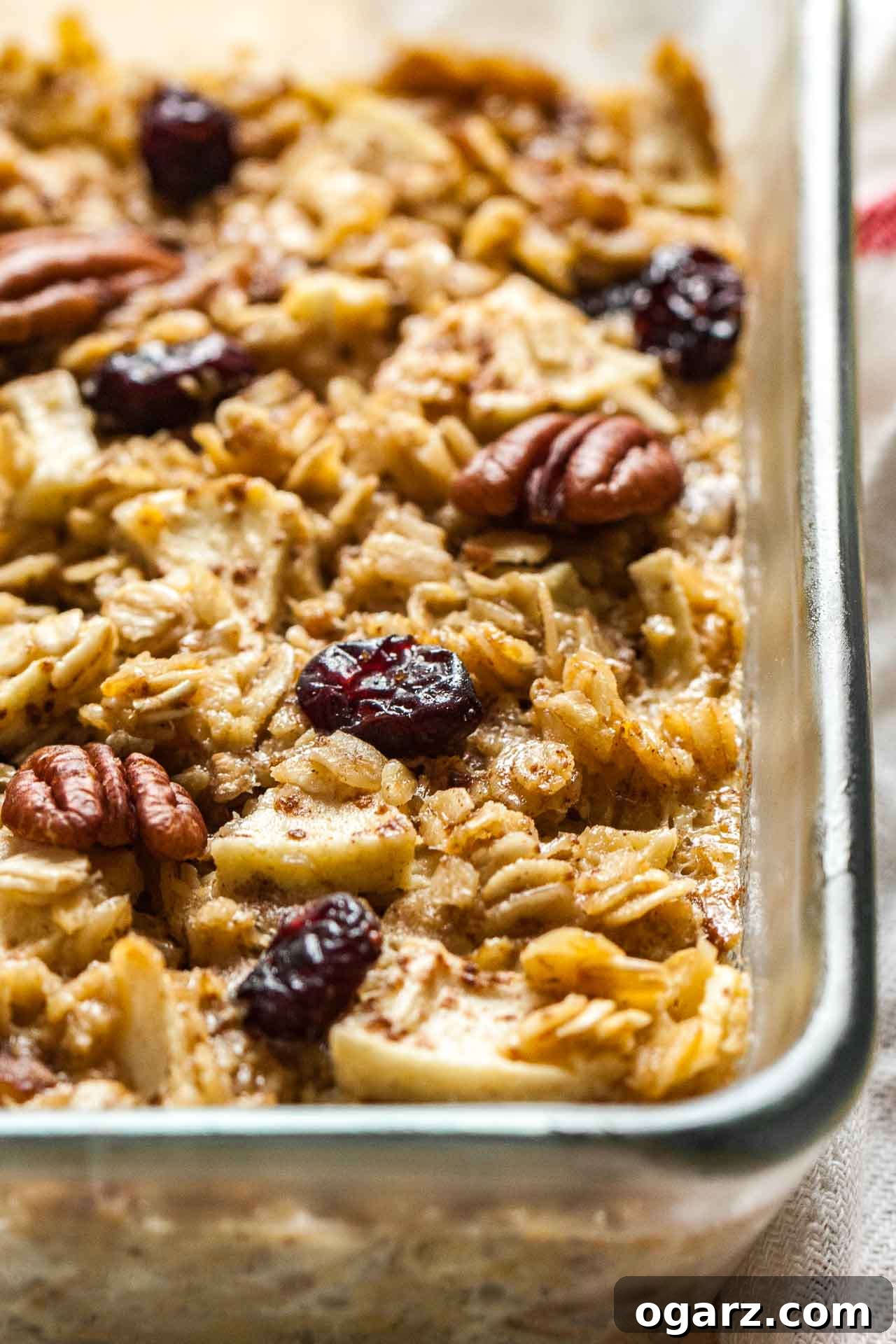 Wholesome Baked Oatmeal 3 Close-up of a glass baking dish filled with golden-brown baked oatmeal, showcasing the apple pieces, pecans, and cranberries.