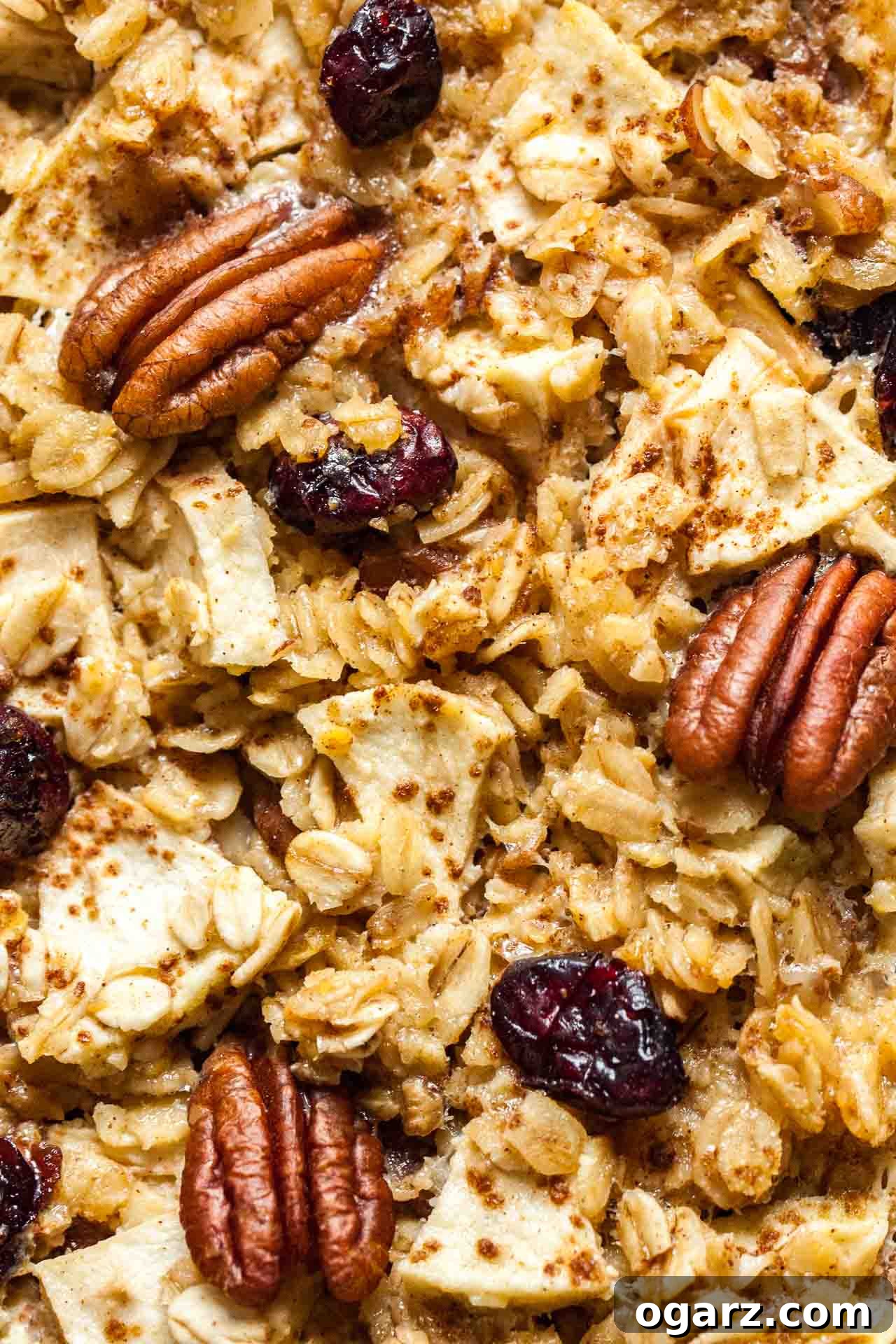 Wholesome Baked Oatmeal 4 Close-up, top-down shot of a serving of baked oatmeal, topped with extra pecans and apple slices, on a wooden board.