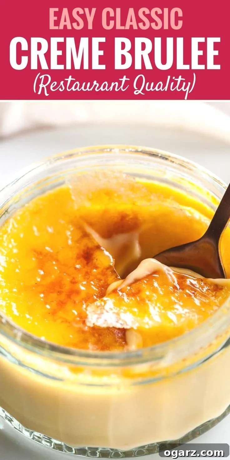 Foolproof Creme Brulee Recipe 10 Close-up of a glass of creme brulee with a bronze spoon cracking its top on a white plate in front of a white dishtowel.
