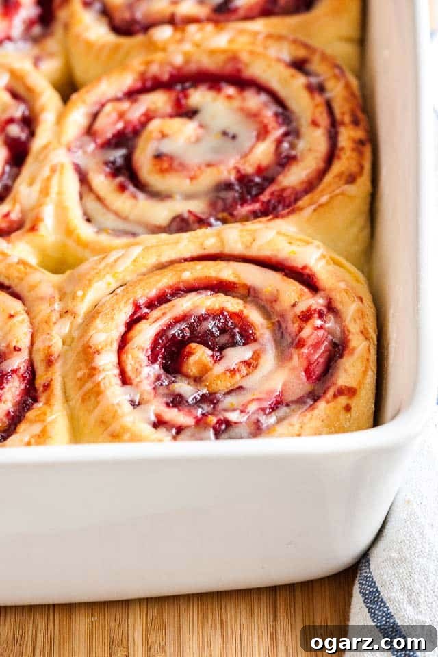 Zesty Cranberry Orange Buns 2 Close-up of a white baking dish with orange cranberry rolls on a bamboo cutting board with a white and blue dishtowel.